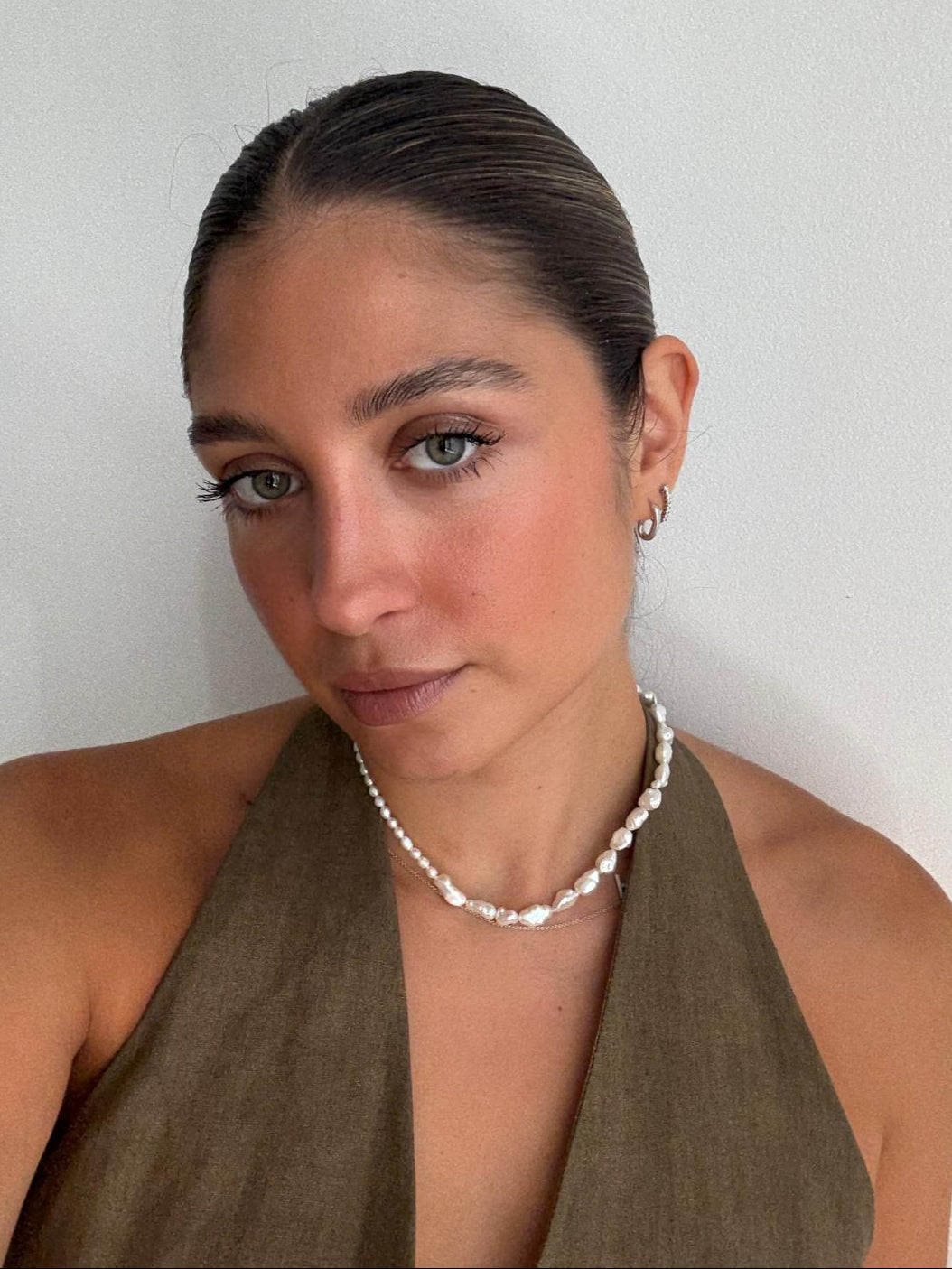 Woman wearing a green halter top and pearl necklace against a plain background