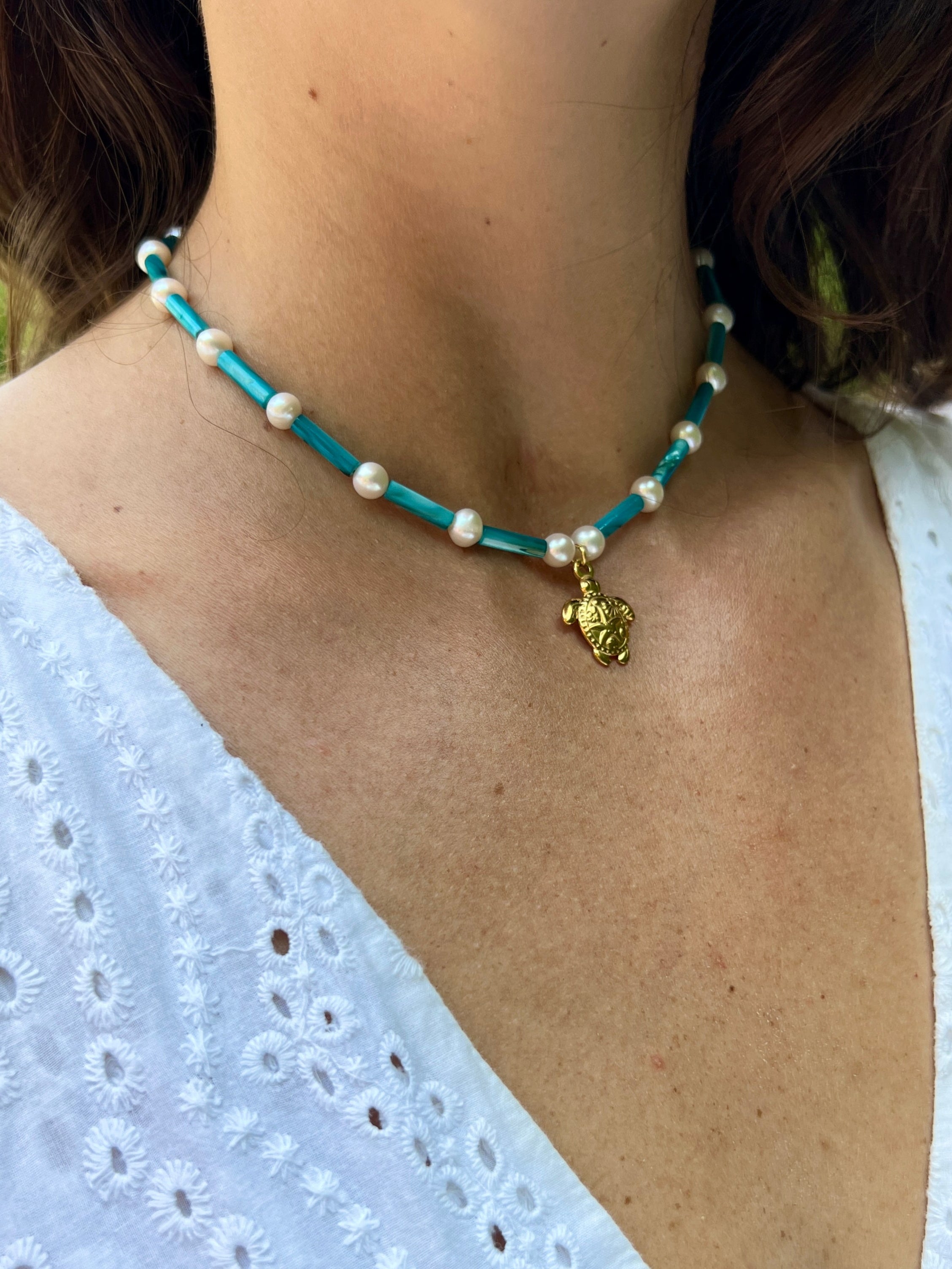 Necklace with turquoise and white beads and a gold pendant on a person wearing a white top.