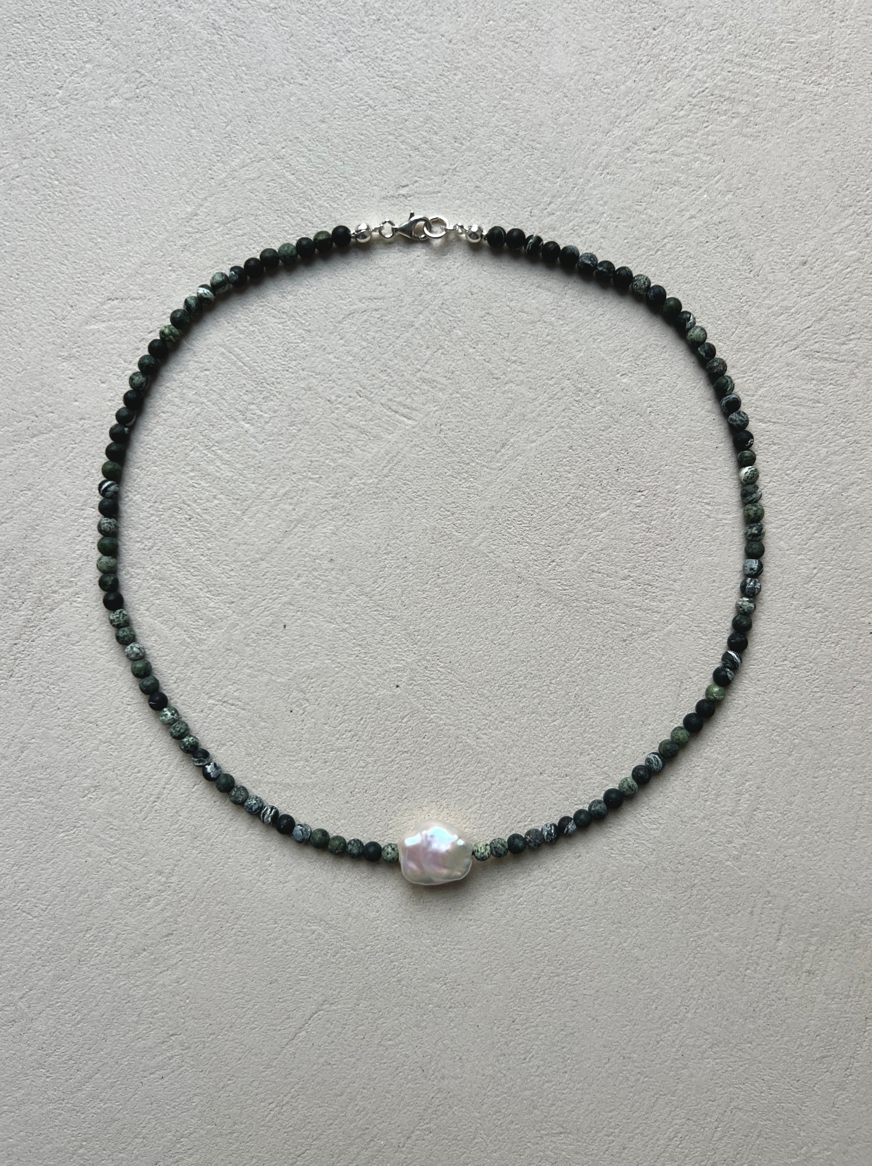 Necklace with serpentine black and green beads and a pearl on a light gray background