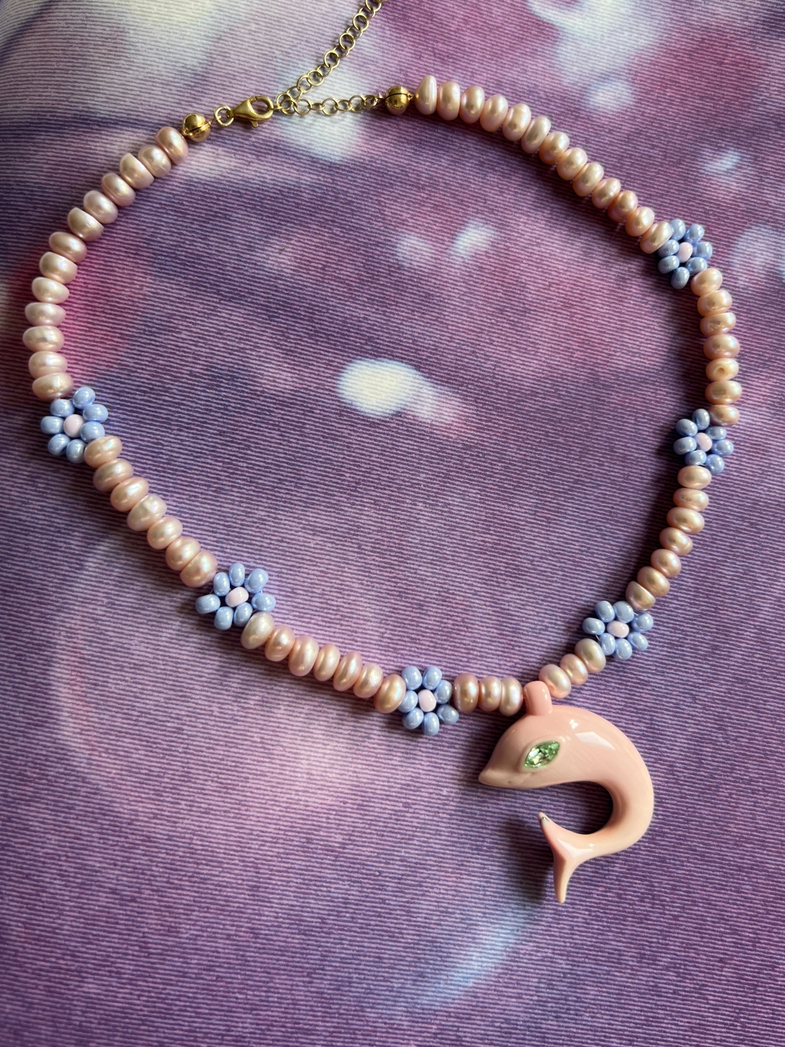Necklace with dolphin pendant and beads on a purple fabric background 