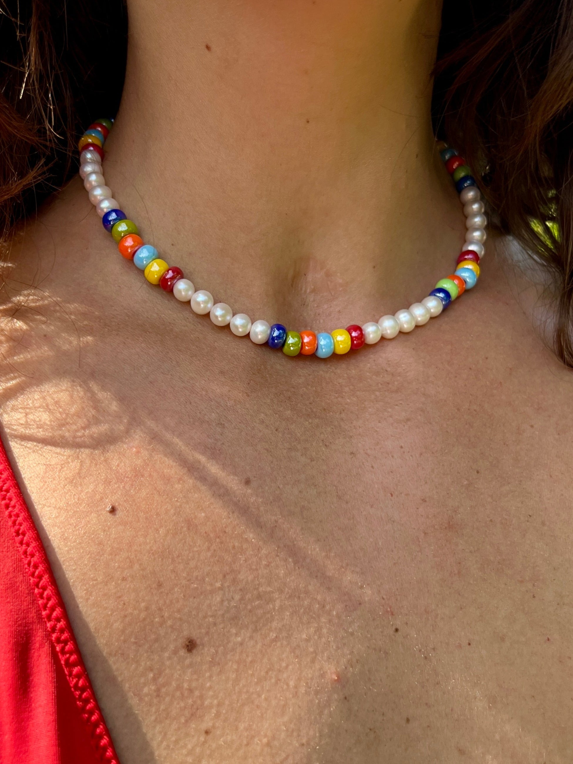 Person wearing a colorful beaded necklace with a red top outdoors