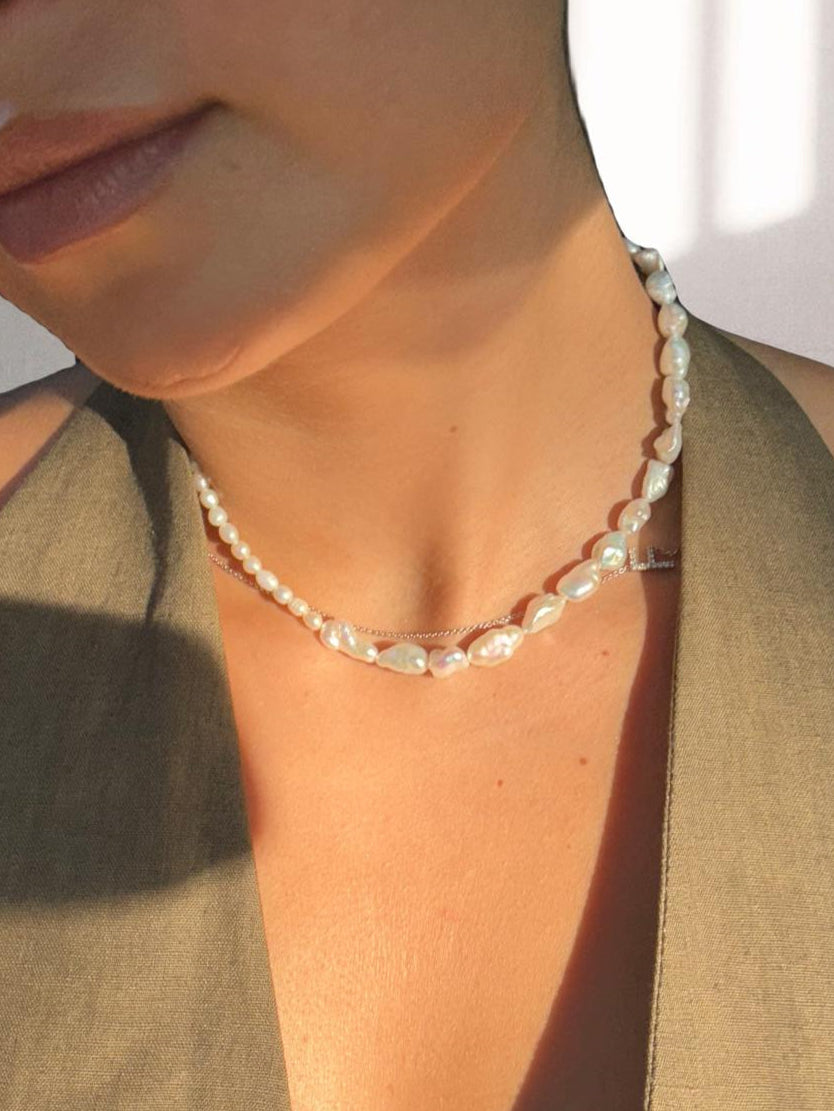 Close-up of a person wearing a pearl necklace with a neutral background